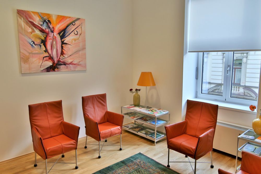 Moderner Warteraum der Ordination Univ. Prof. Dr. Hans Rabl mit orangefarbenen Stühlen und einem abstrakten Gemälde an der Wand.